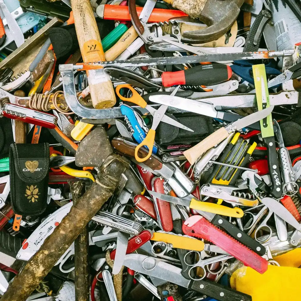 A chaotic pile of assorted tools including scissors, hammers, knives, and screwdrivers, representing disorganisation or overload.